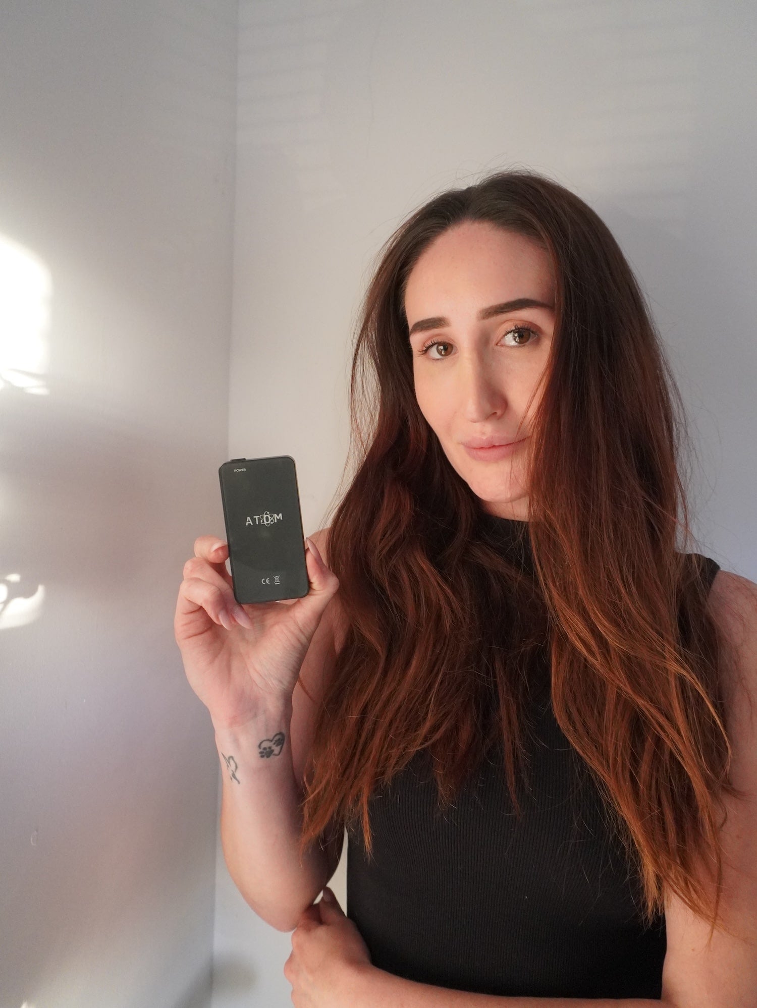 Woman holding a digital emf blocker with a black case against a plain background
