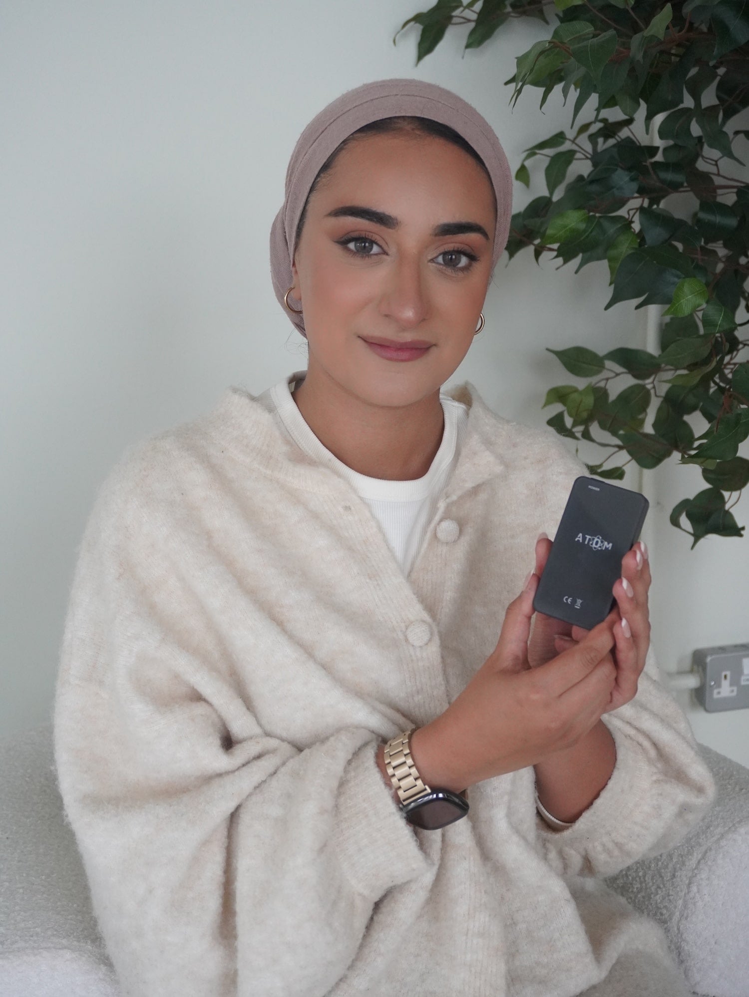 Woman holding a digital device with a plant in the background.