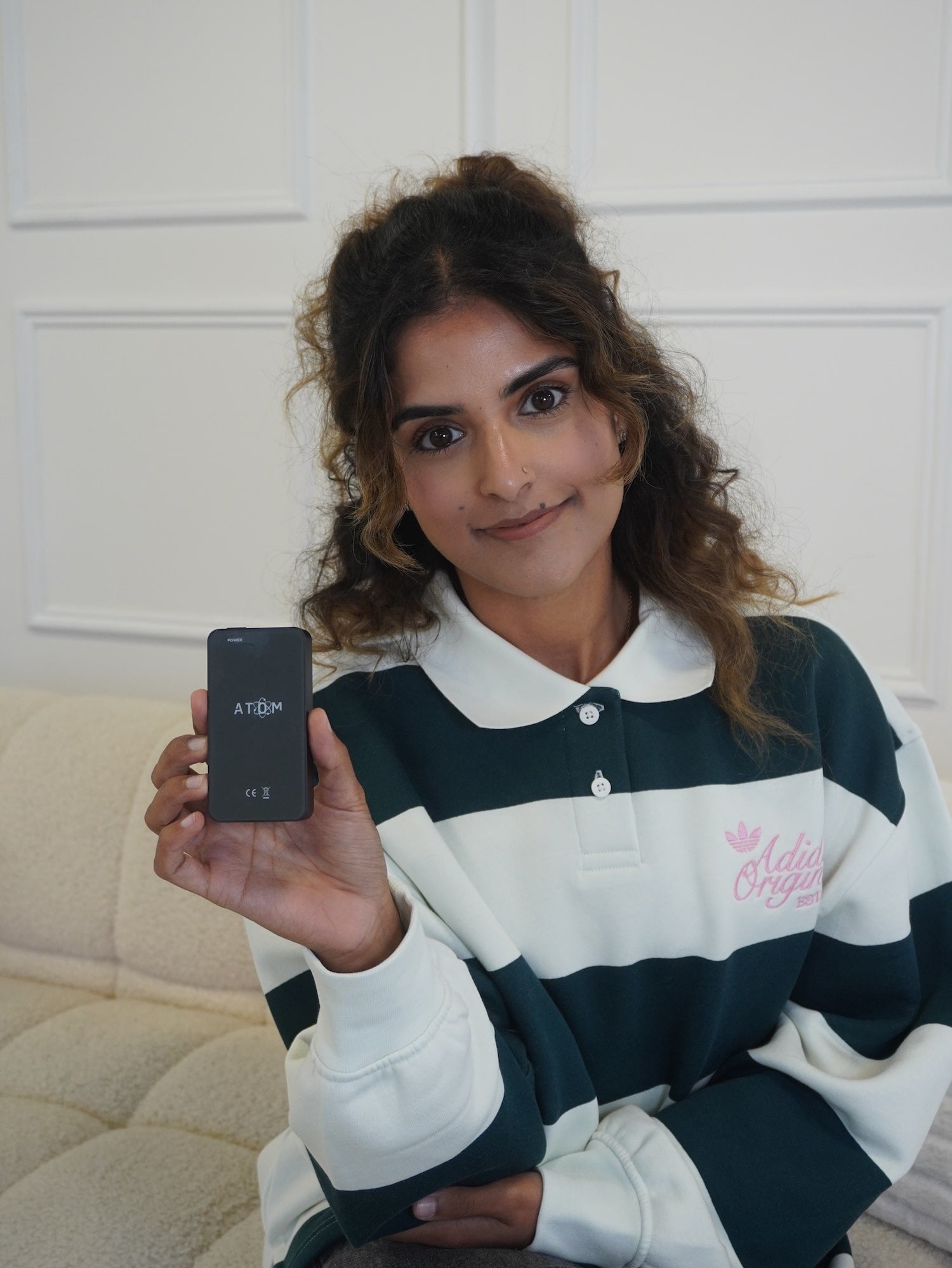Woman holding a frequency device with a white wall in the background.