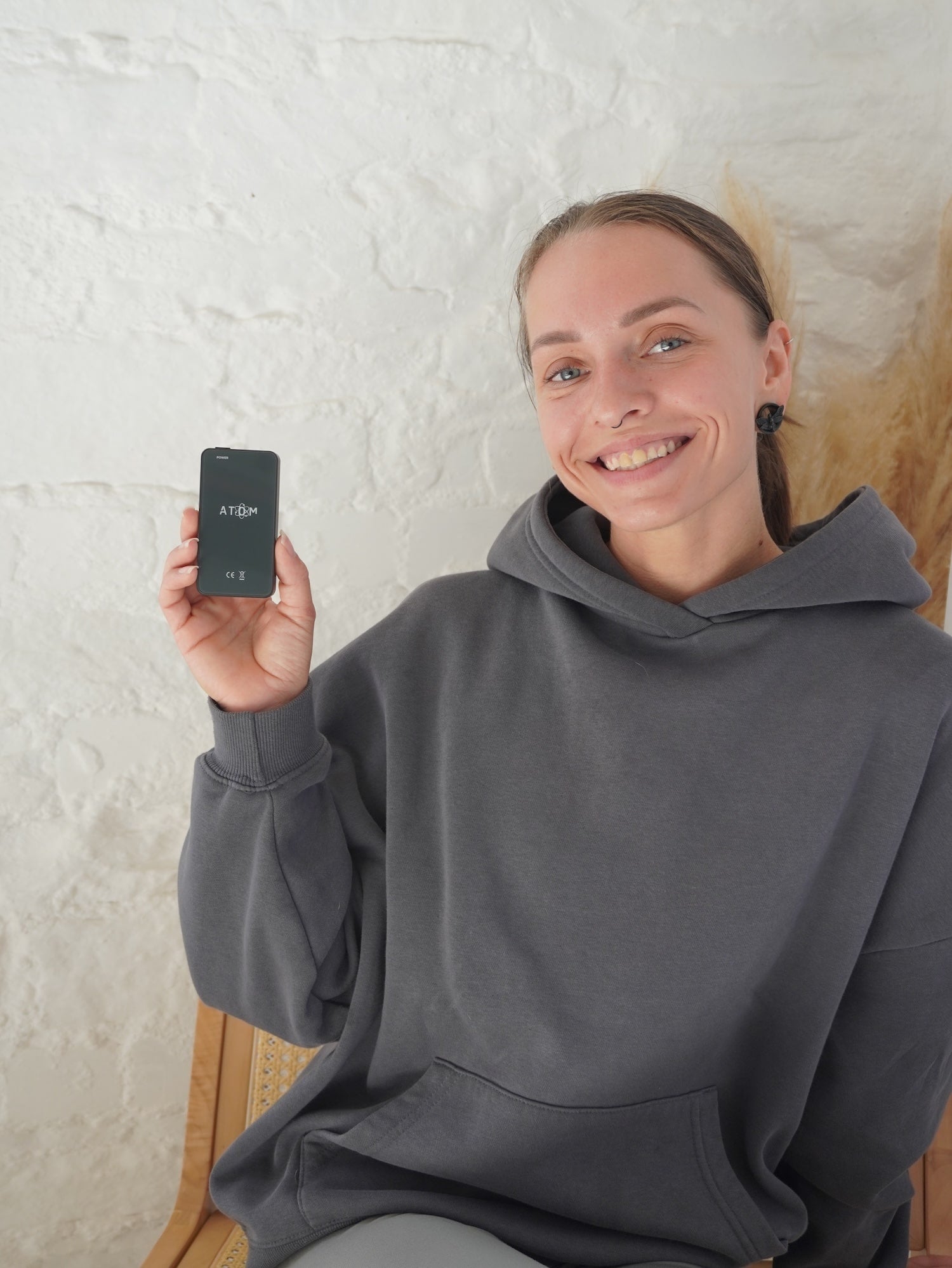 Person wearing a gray hoodie holding a frequency device with a white wall in the background.