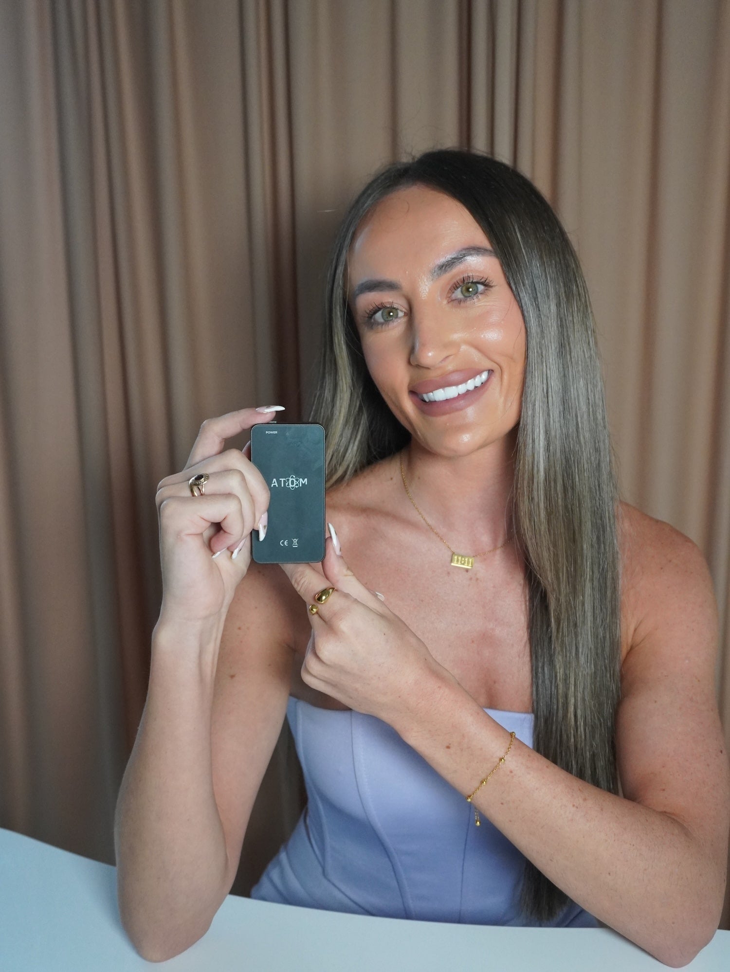 Woman holding a frequency device with a coloured curtain in the background.